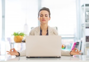 Business woman meditating near laptop in office, achieving workplace bliss.