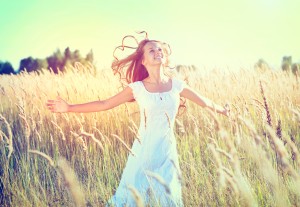 Beauty Girl Outdoors enjoying nature. Beautiful Teenage Model girl in white dress running on the Spring Field, Sun Light. Glow Sun. Free Happy Woman. Toned in warm colors.