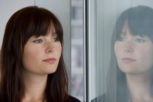 A young woman looks at her reflection in the eye saying "I love you", building up a healthy relationship with herself.