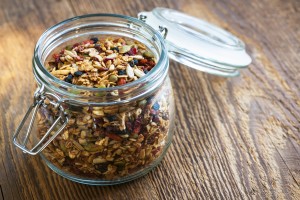 Homemade granola in open glass jar on rustic wooden background