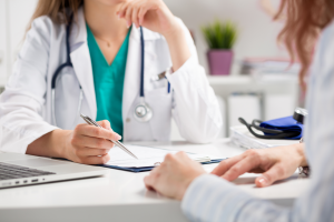 A medical professional speaking to a patient while writing on a pad of paper