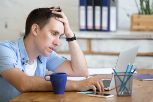 A young man looking bored while staring at a laptop